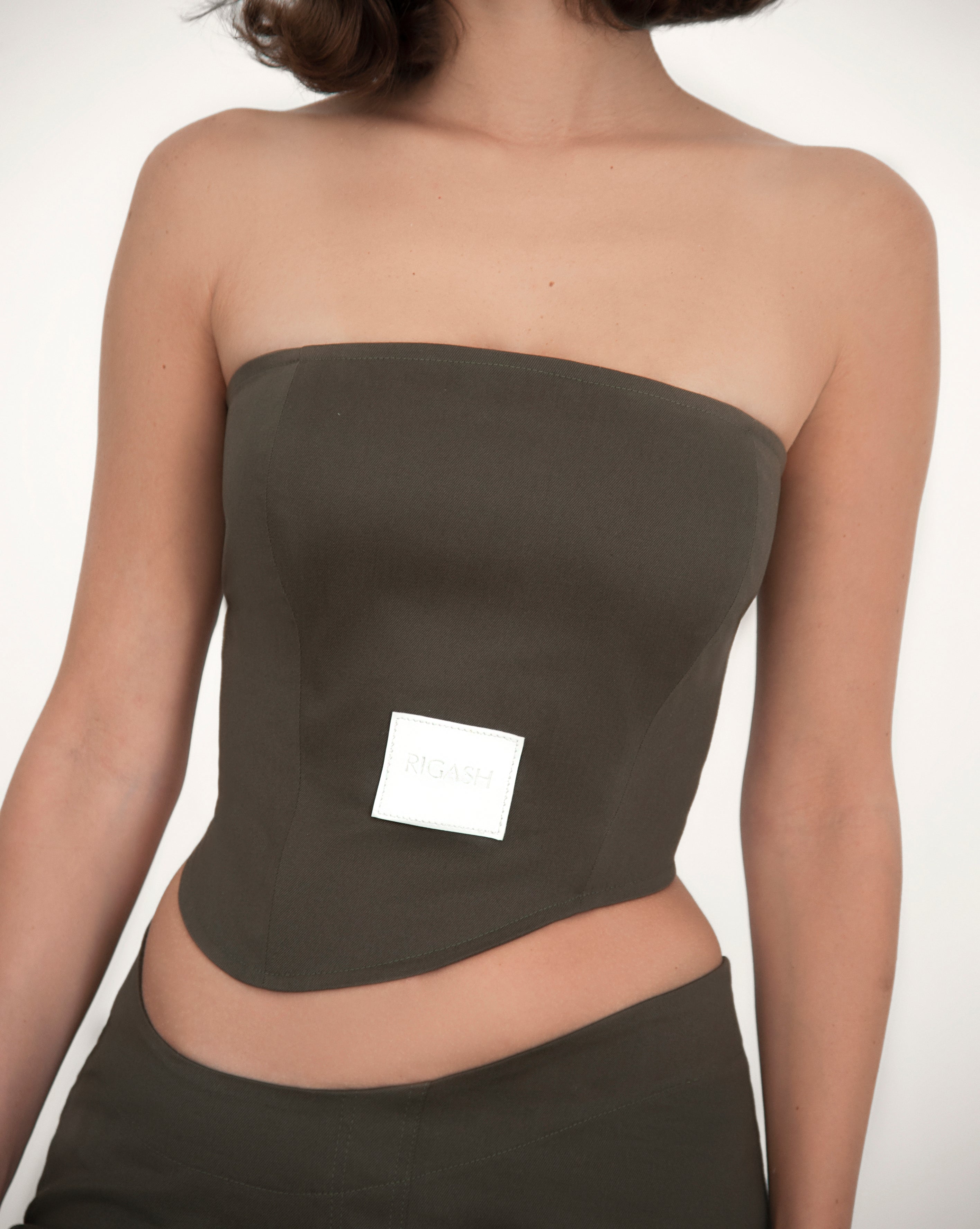 Asymmetrical corset top with a round strapless neckline. Back panels held together by brown leather belt. Visible front leather tag with embossed logo print. 
